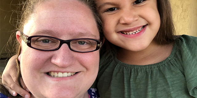 A woman in glasses smiles next to her young daughter