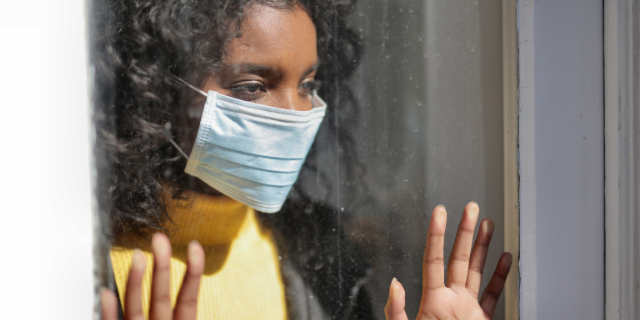 A woman wearing a medical mask looks out a window
