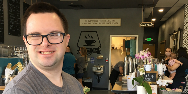 A young man smiles in a coffee shop