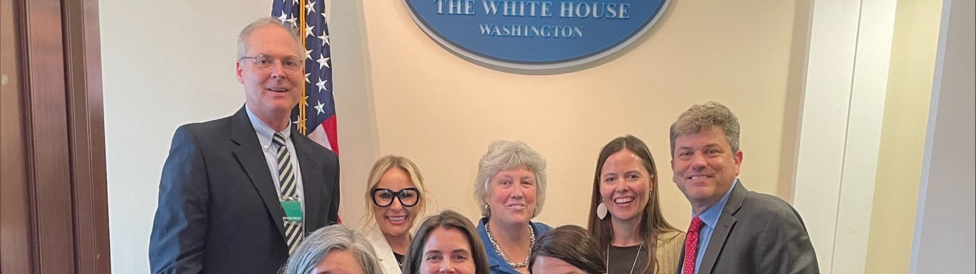 A group of people smile by a sign at The White House